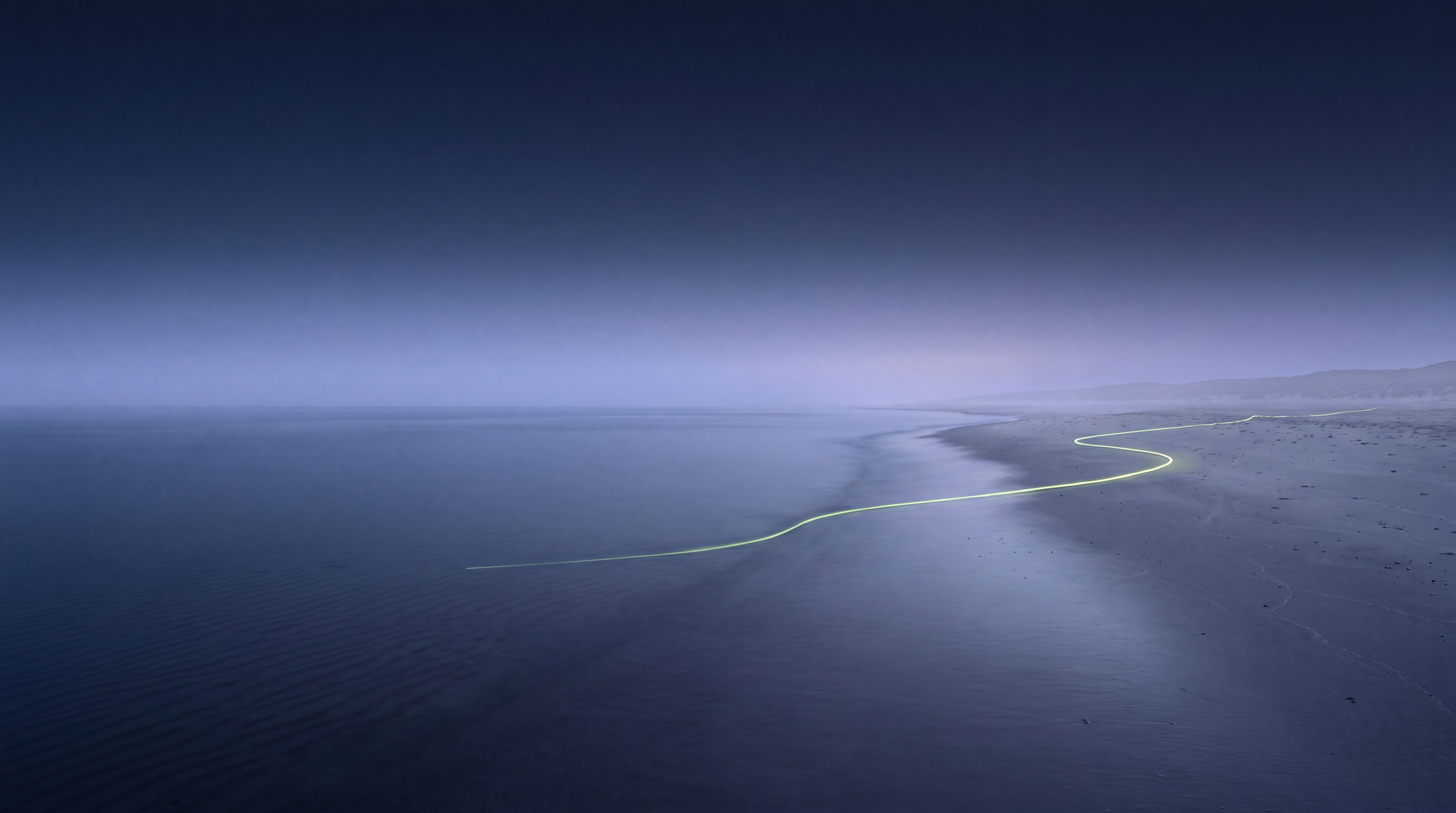 Küstenlandschaft vor Sonnenaufgang: ein einzelnes, schwach limonengrün leuchtendes Datenkabel steigt aus dem dunklen Meer und läuft über den Sand landeinwärts.